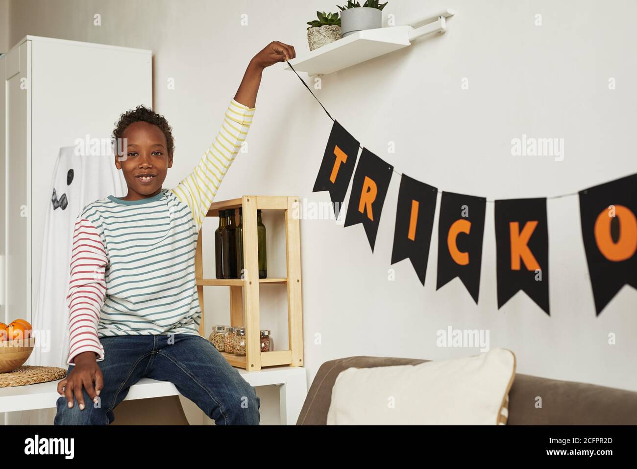 Cheerful African American boy wearing casual clothes decorating room for Halloween party, copy space Stock Photo