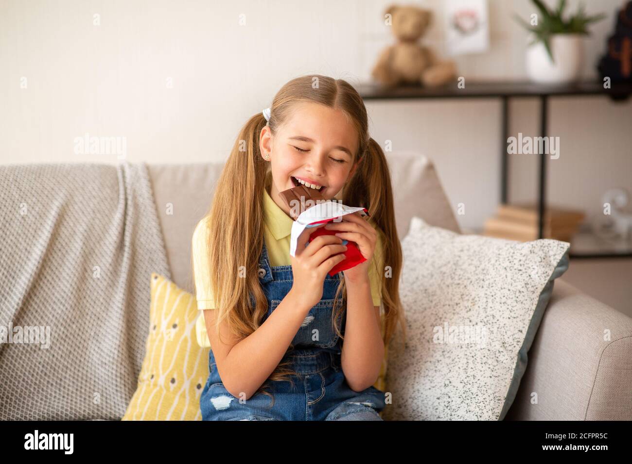 Girl eating chocolate sitting on a couch at home Stock Photo