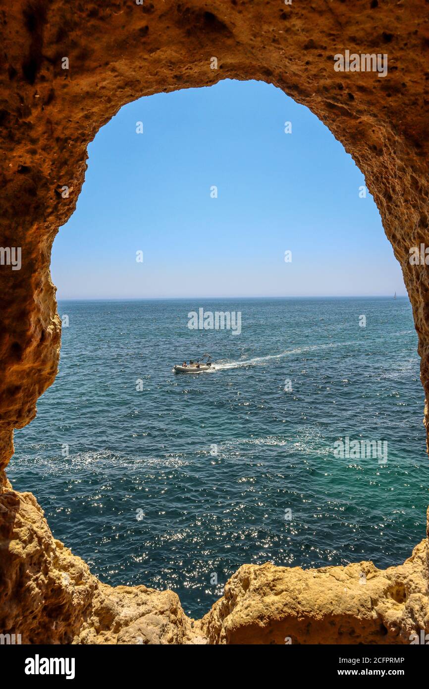 A picture of a rock window in Algar Seco Algarve, Portugal with a view of an turquoise ocean with a boat Stock Photo