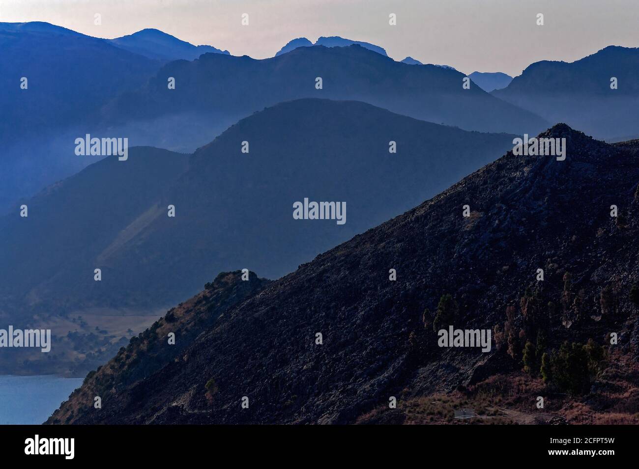 Setting sun throws details of boulder-strewn hillside above Lago Rosamarina in Sicily, Italy, into contrast against more distant peaks and rugged ridges. Stock Photo