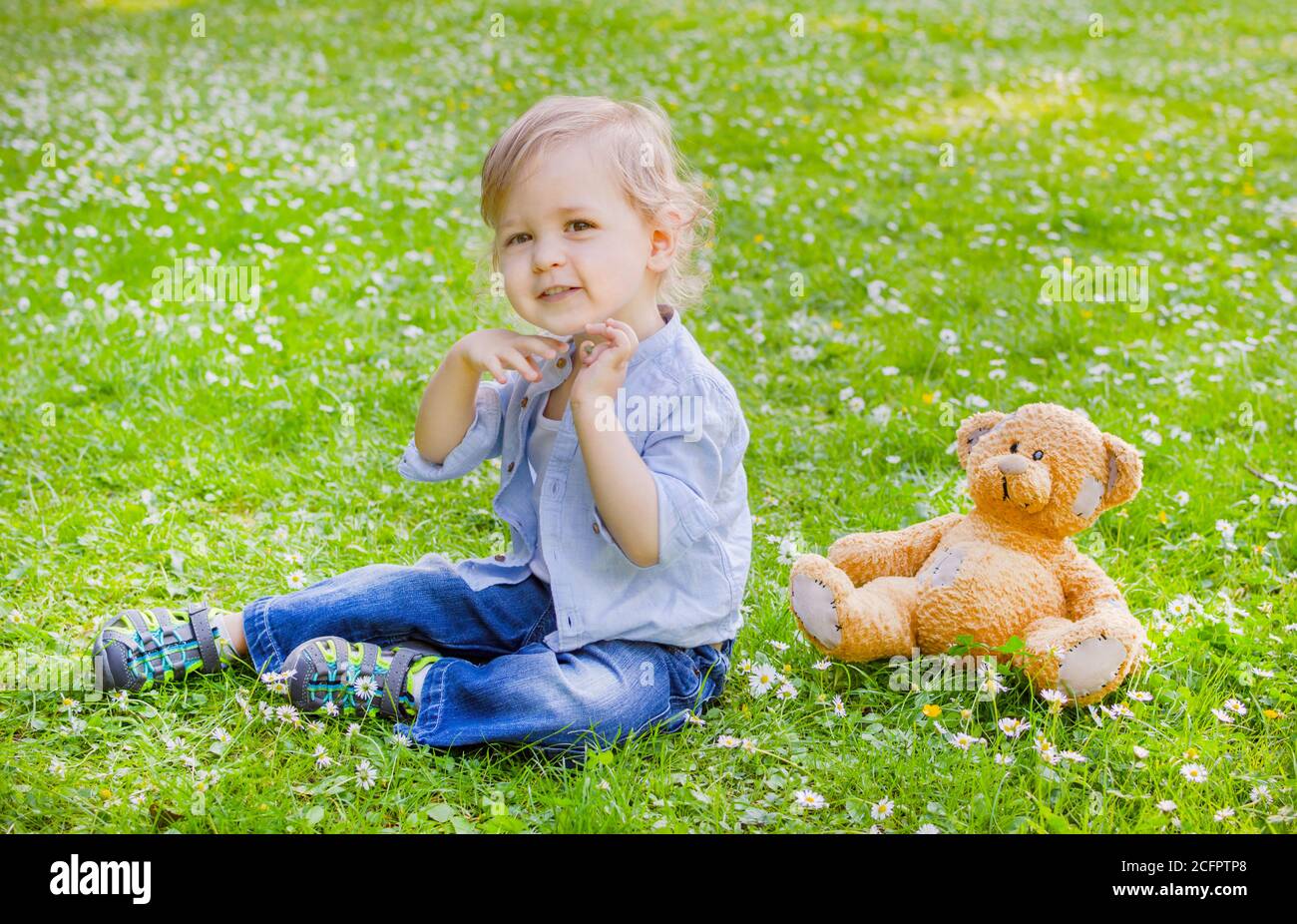 Cute little child standing on the grass in the park with his teddy bear ...