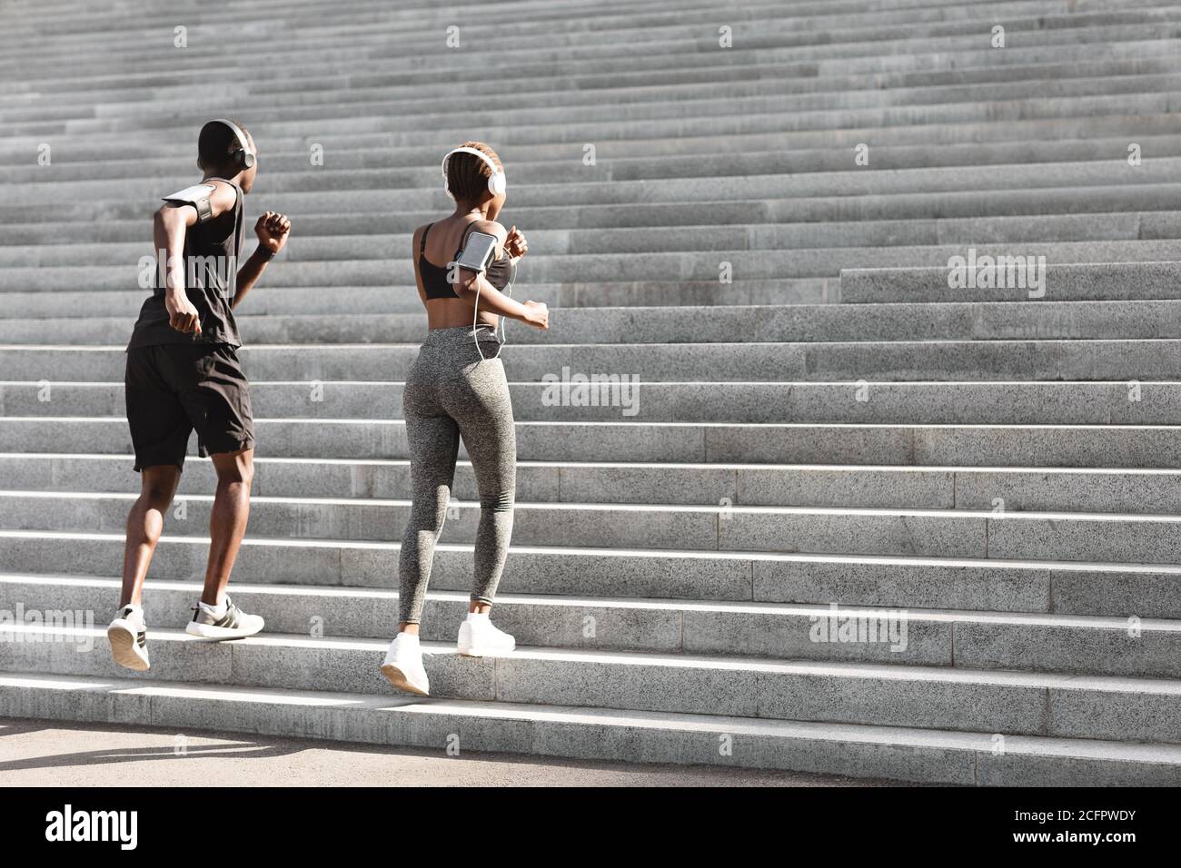Couple Of Sporty Black Joggers Running Up The Steps In Urban Park Stock Photo