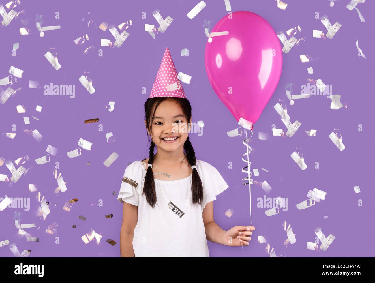 Asian Girl Holding Balloon Standing Under Falling Confetti In Studio Stock Photo