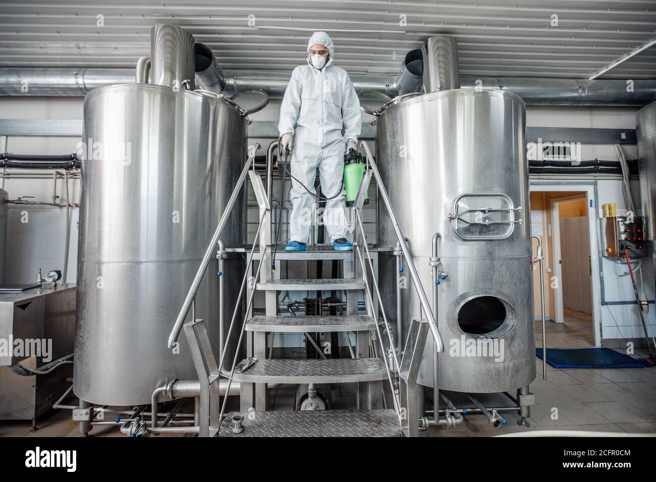 Cleaning and disinfection of brewing kettles. Man in hazmat suit with