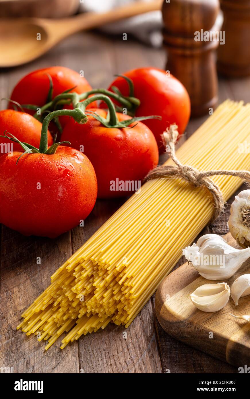 Raw spaghetti pasta tied in a bundle with fresh vine tomatoes and garlic on a rustic wooden table Stock Photo