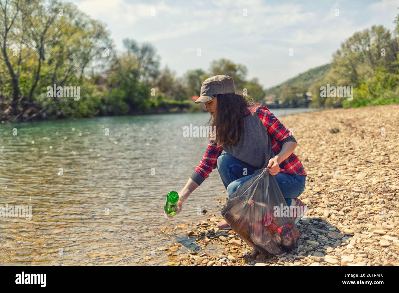 A woman volunteer pulls a bottle out of the water, during the event to clean the river Bank. Earth day and environmental improvement concept. Stock Photo