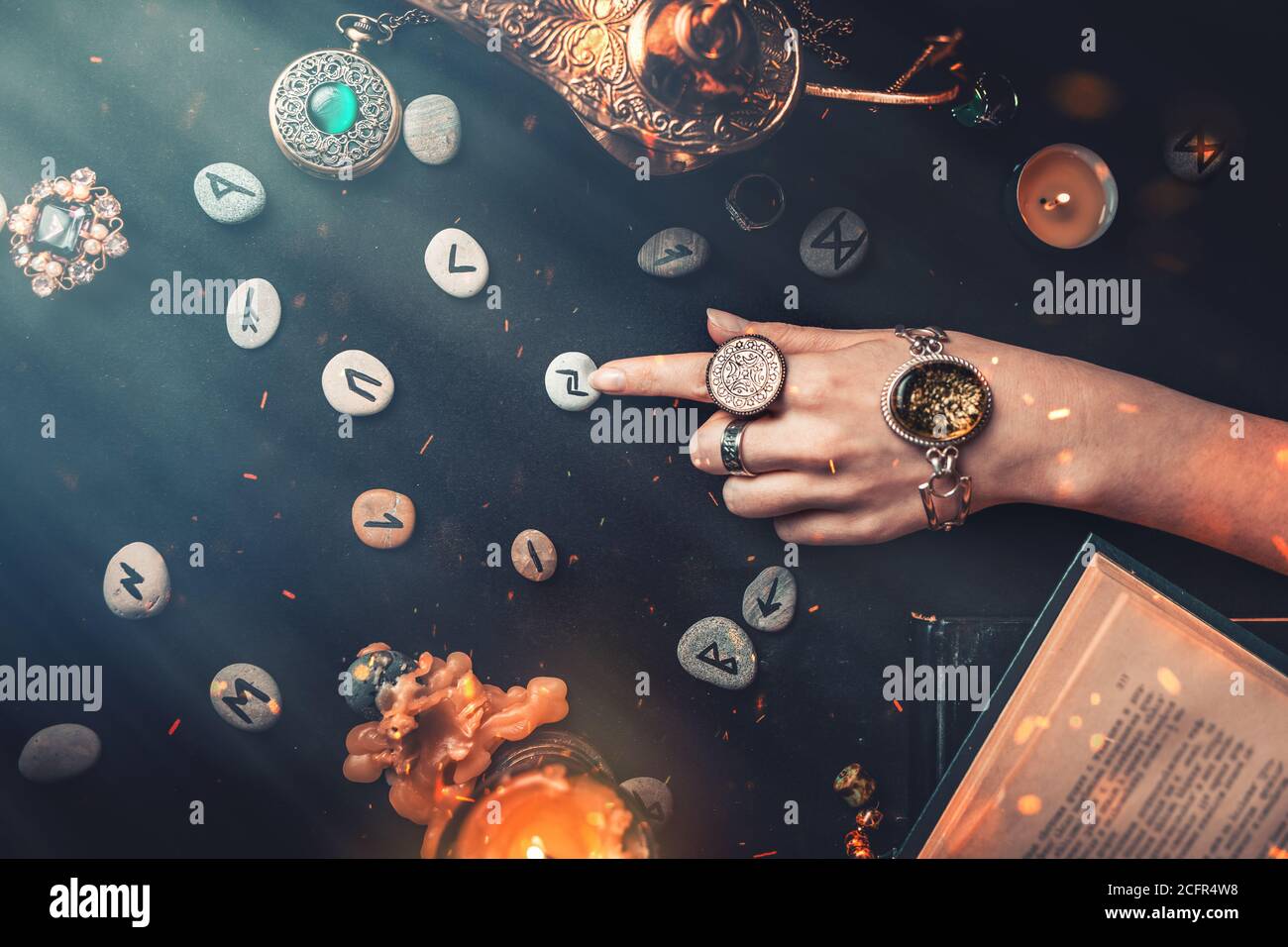 Astrology and esotericism. The witch's female hands point to the Runestone with her finger. On a black background lie fortune-telling runes, amulets, Stock Photo