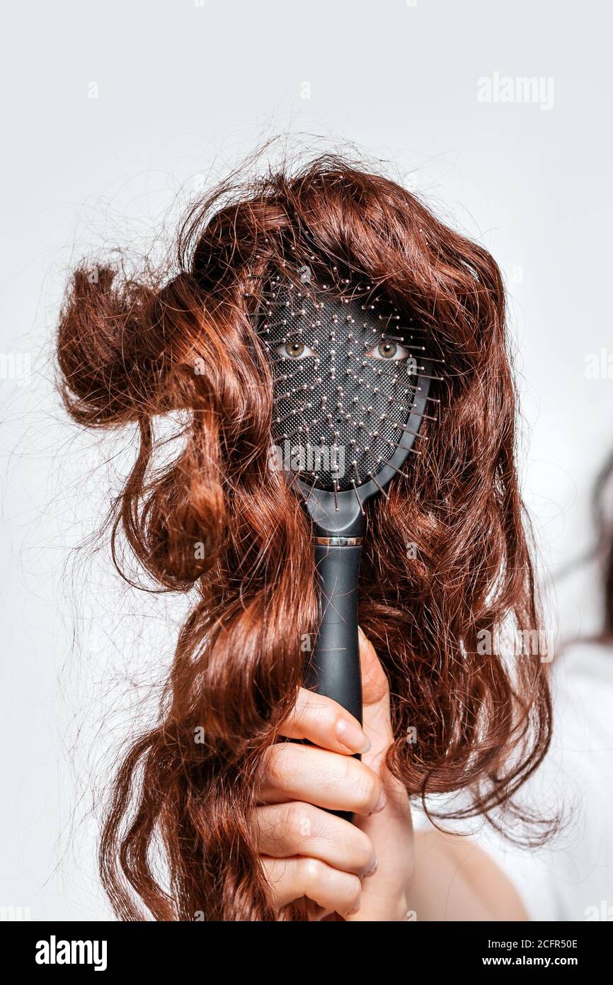 A woman's hand holds a comb with eyes and a wig that imitates a person's face. Hair care concept. Stock Photo