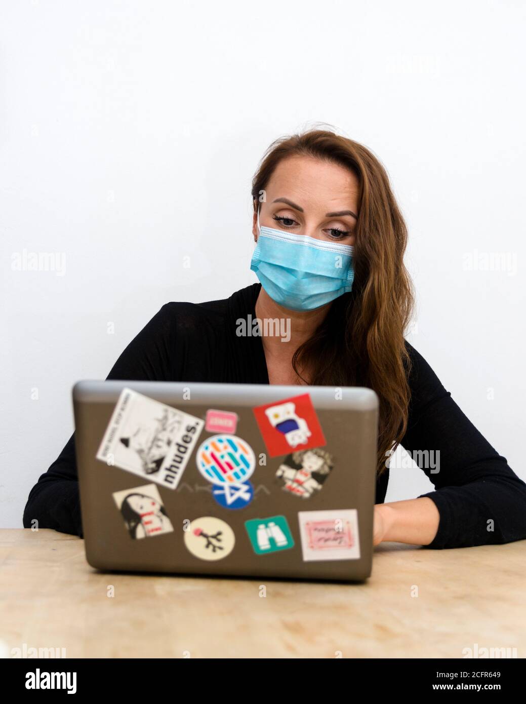Woman working on a laptop while wearing a protective face mask Stock ...