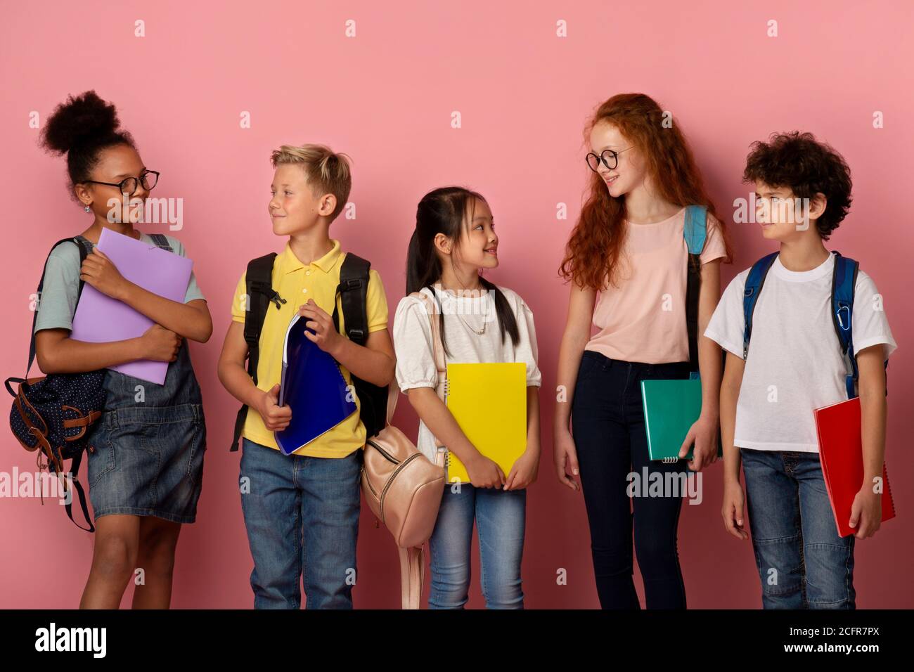 Adorable schoolkids of different races and ages looking at each other over pick background Stock Photo