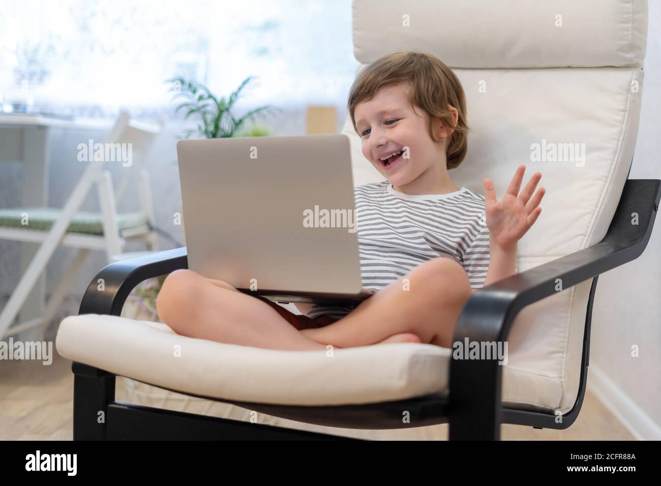 Happy kid boy sit on computer using laptop and having a video call ...