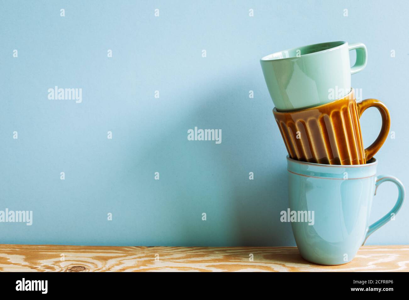 Stack of ceramic mug cups on wooden table with blue background Stock Photo