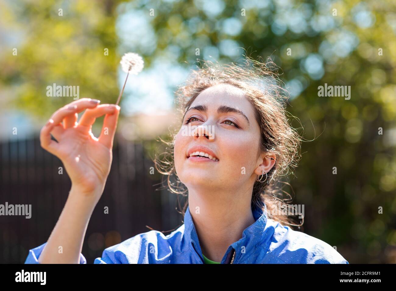 Spring and happiness. Portrait of a Young woman holding a dandelion and looking at it with a smile. Stock Photo
