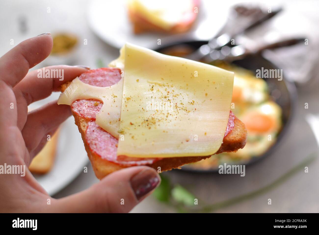 Delicious fast food breakfast. Crispy Toast with cheese and sausage. Sandwich in a white plate Light background. Minimalistic food photo. A woman Stock Photo