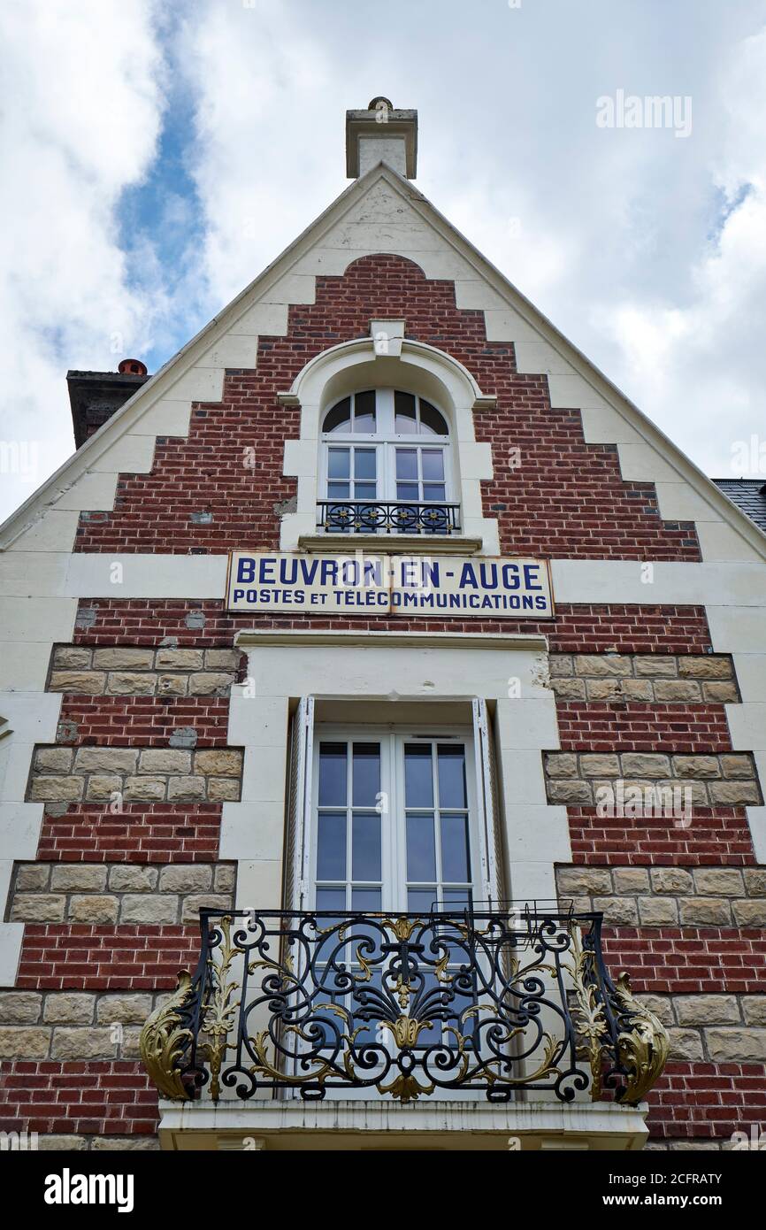 Red brick facade with signboard of the former french post & telephone companies building at Beuvron-en-Auge with 2 windows and an ornate metal balcony Stock Photo