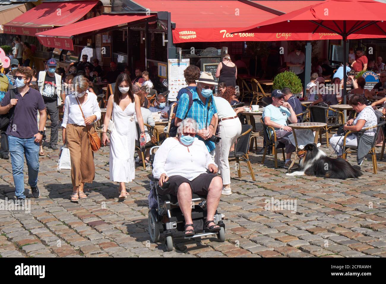 Man in wheelchair and other holidaymakers wearing facemasks during the COVID-19 pandemic in the picturesque harbour town of Honfleur in Normandy Stock Photo