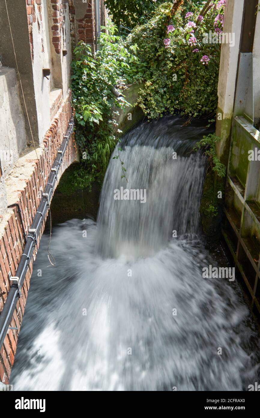 Small water cascade gushing into a stream at chateau de Breuil in Normandy, France Stock Photo