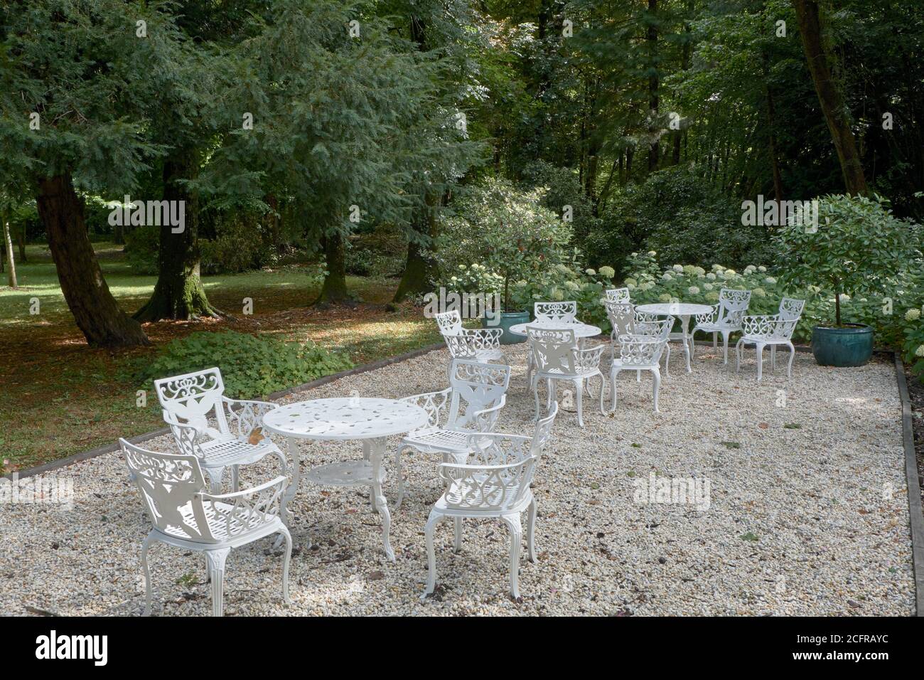 White painted metal tables and on a gravel terrace chairs in a garden setting at Château de Breuil in Normandy, France Stock Photo