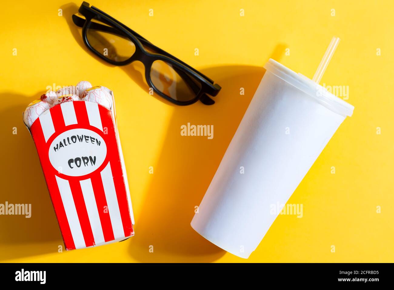 Accessories for watching films and movies at home - glasses, Halloween corn in the shapes of eyeballs and paper cup with drink on a yellow background, Stock Photo