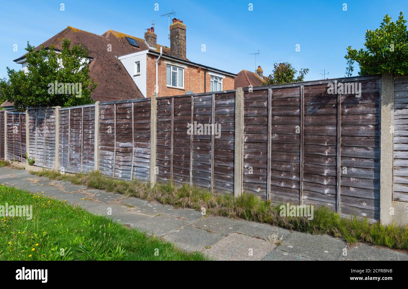 Wooden garden boundary fence using horizontal Waney, AKA Overlap & Larch Lap style wood panels, strengthened by concrete pillars in England, UK. Stock Photo