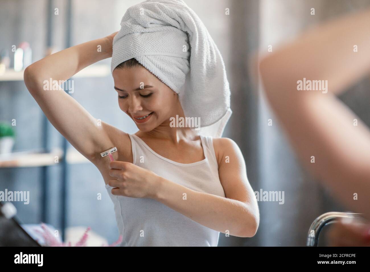 Pretty Caucasian woman shaving her underarm with razor near looking