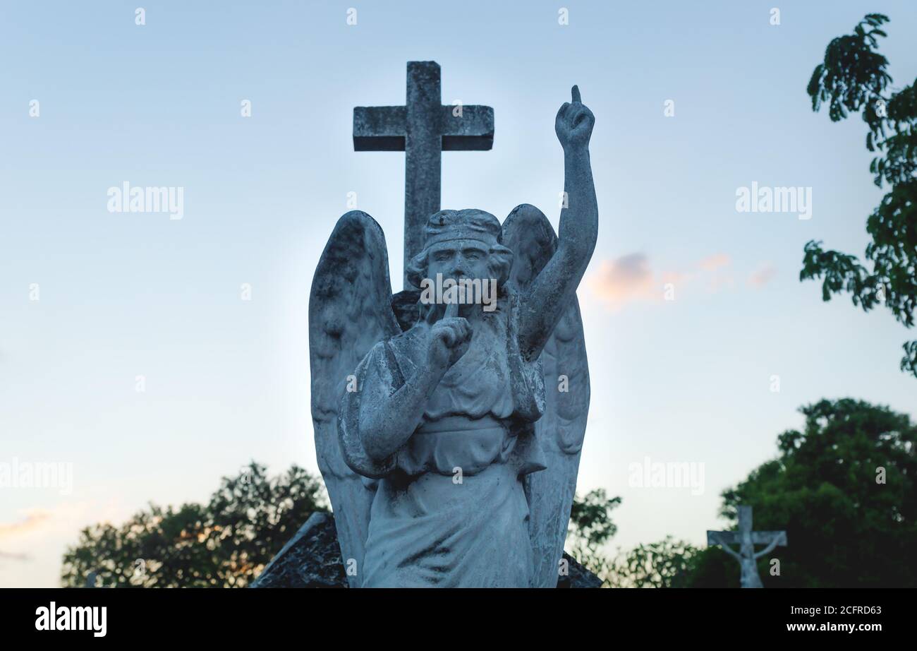 Stone angel statue with a silence sign and pointing up to heaven during sunset at the cemetery 'Cementerio General' in Merida, Yucatan, Mexico Stock Photo