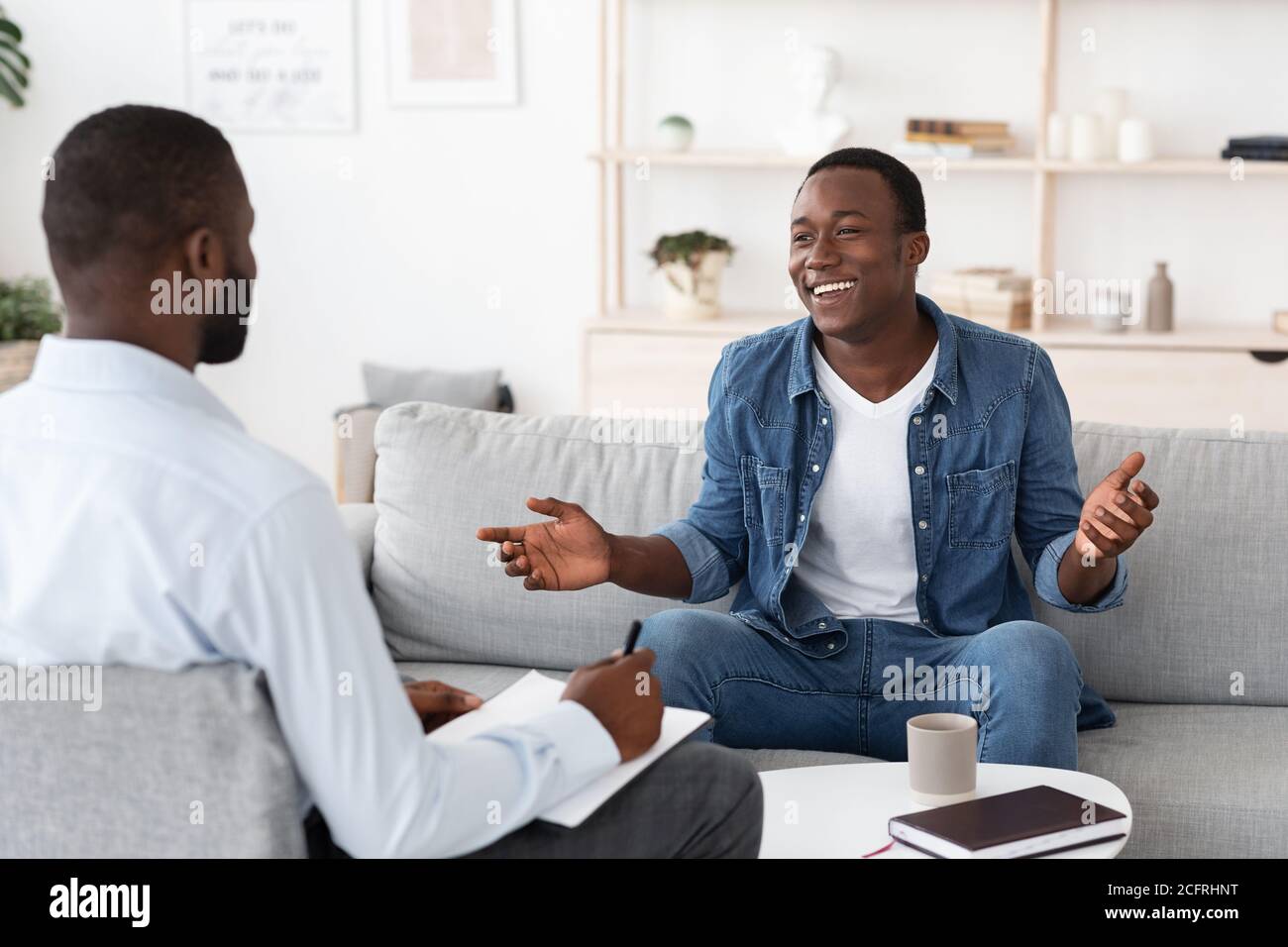 Successful Therapy. Cheerful black man talking to psychologist at his office Stock Photo