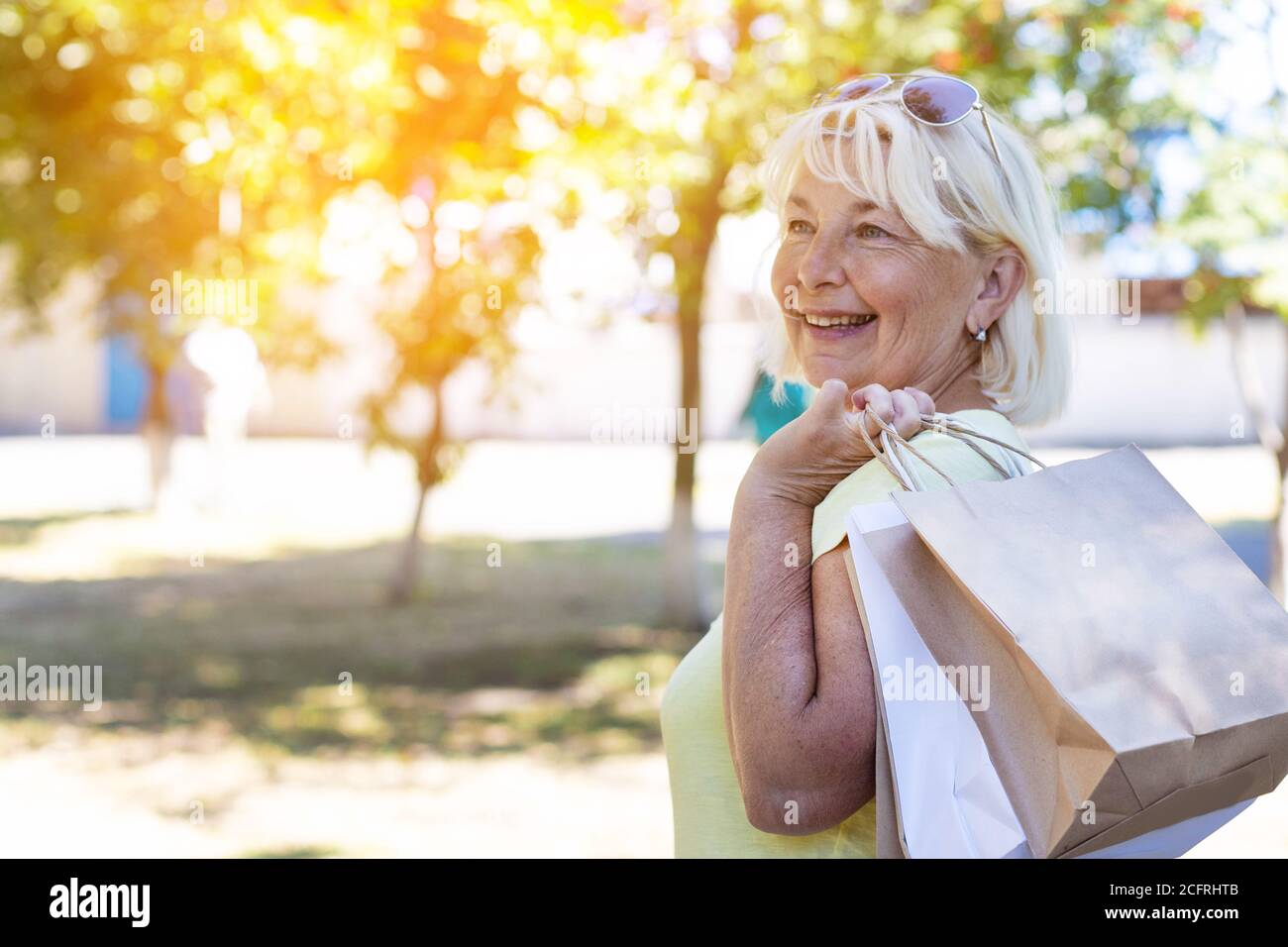 Beauty blonde smiling girl in sunglasses with shopping bags in the park on a sunny day. Shopping concept Stock Photo