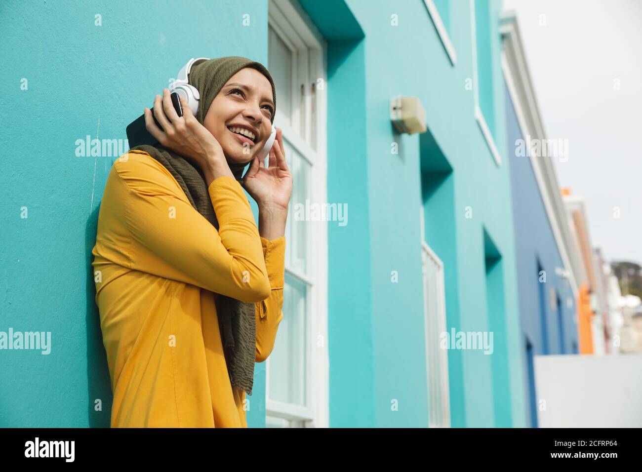 Woman in hijab listening to music using headphones outdoors Stock Photo