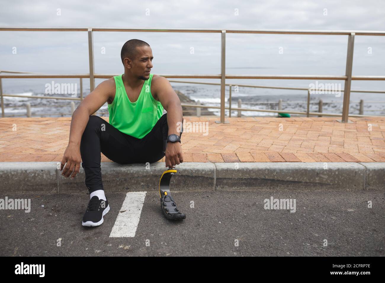 Man with prosthetic leg sitting on footpath Stock Photo
