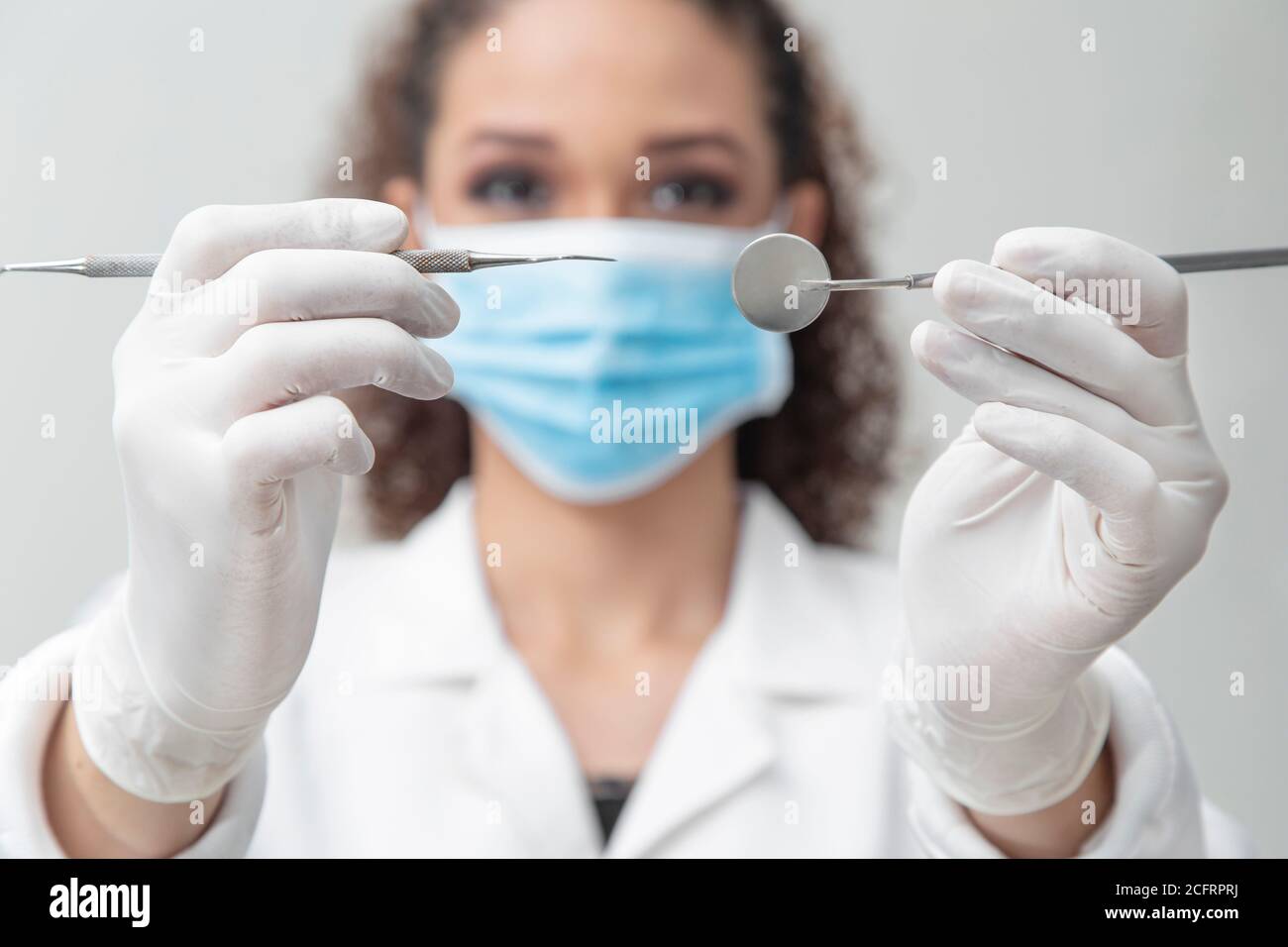 dentist face with mask, gown and cap holding medical instruments, close up Stock Photo