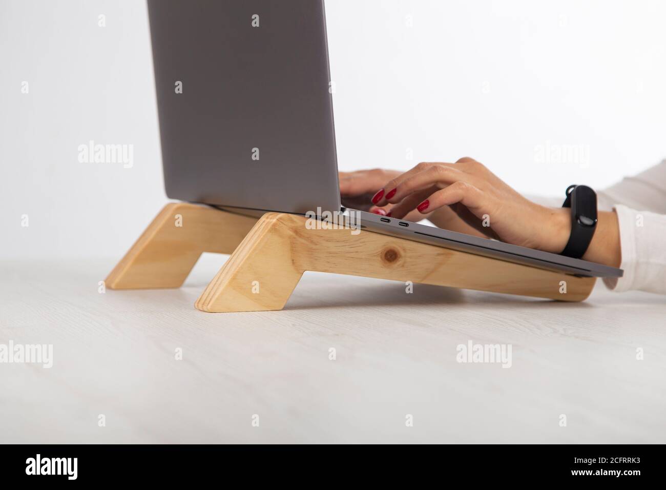 hands of a woman typing on a gray laptop with a wooden stand on a desk Stock Photo