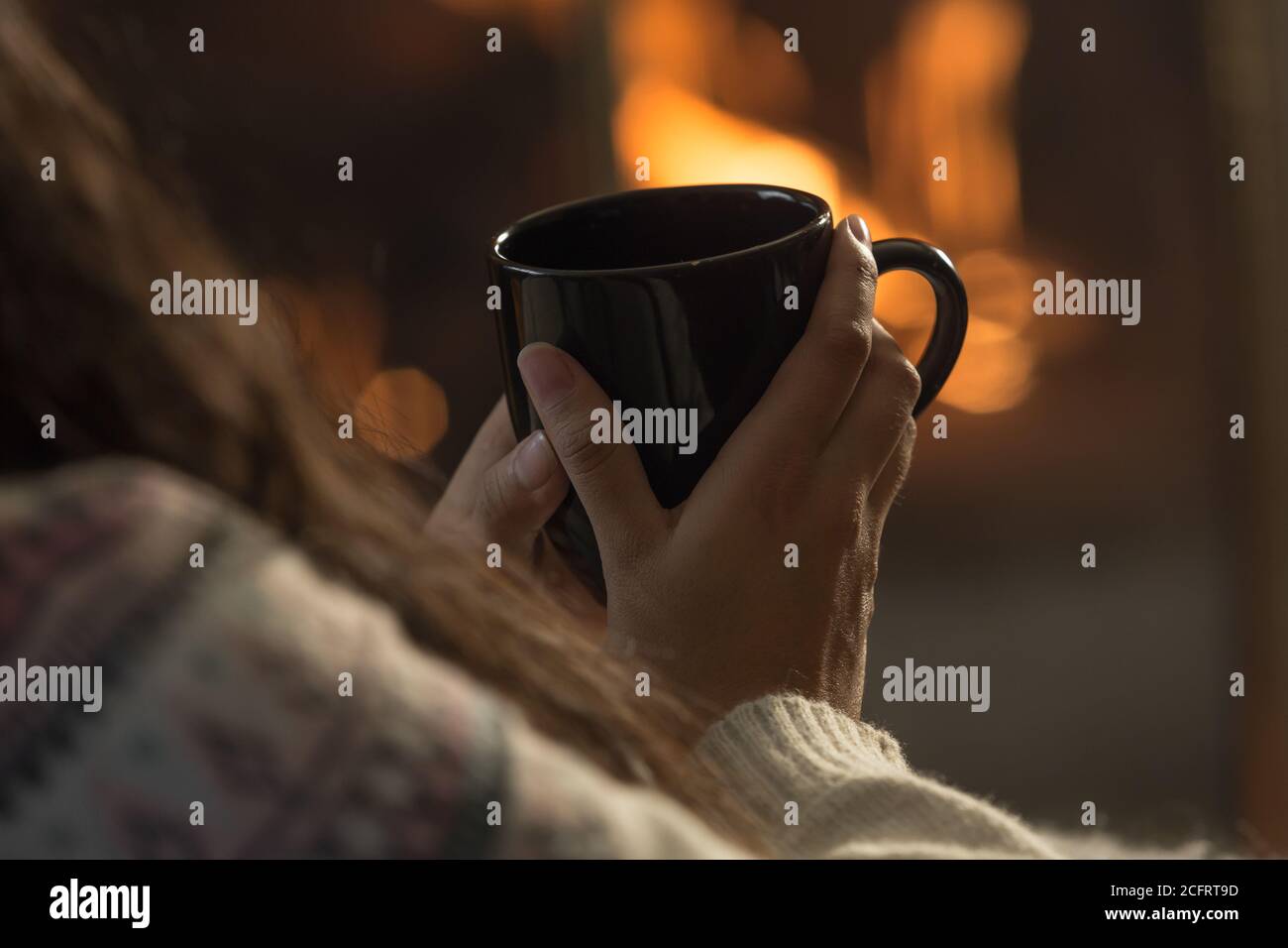 black mug in hands with lit fireplace background Stock Photo