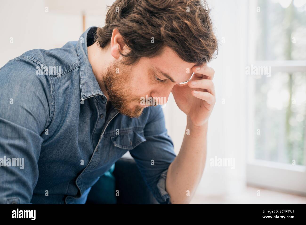 Thoughtful pensive serious male sitting on the sofa at home Stock Photo