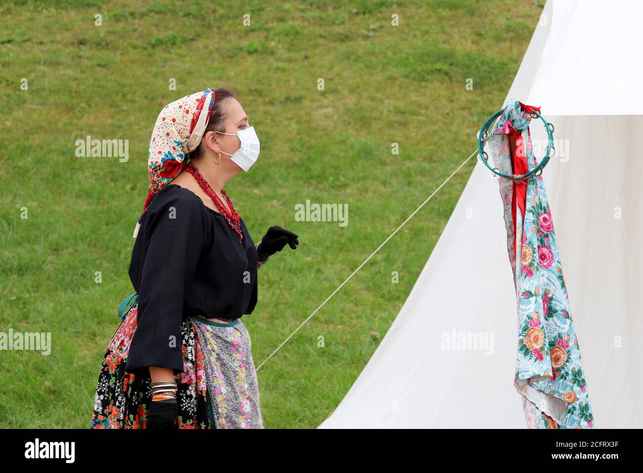 Roma woman in face mask and protective gloves in gypsy camp during historical festival. Safety during the coronavirus pandemic Stock Photo