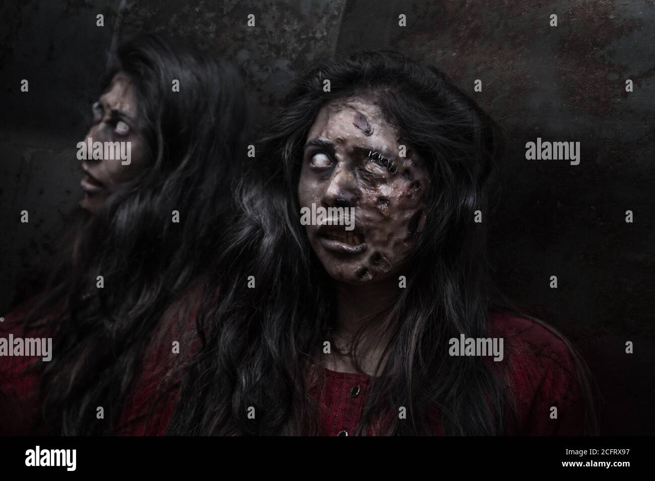 woman with long hair disguised as a zombie, reflecting in a mirror, with dark background, horror Stock Photo