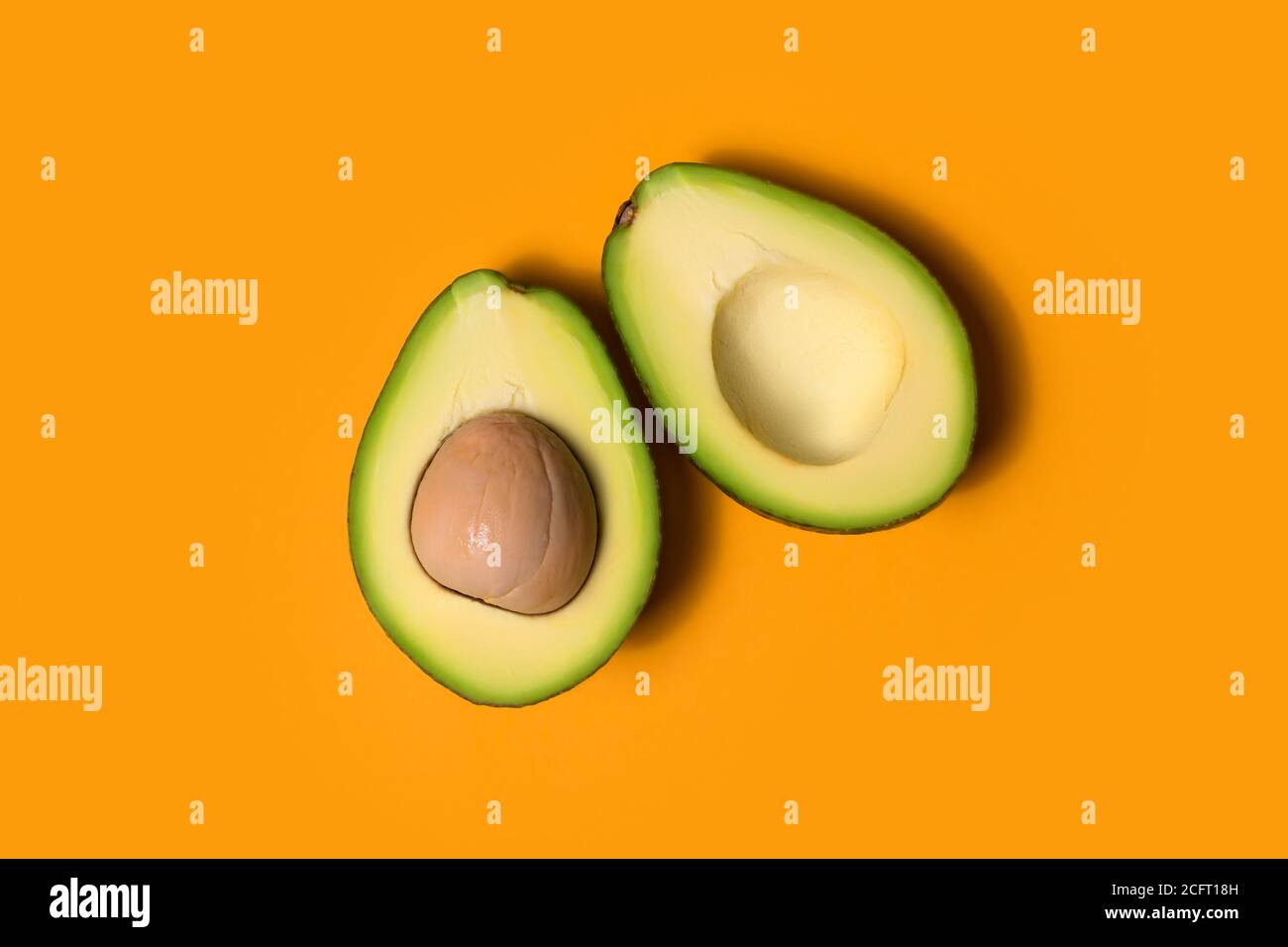 Two halves of ripe avocado on an orange background Stock Photo