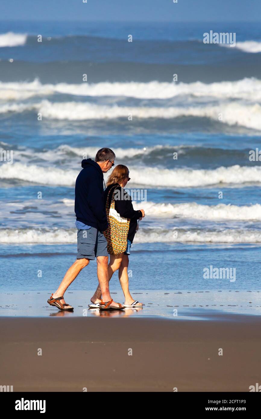 Older couple walking on the beach next to the pacific ocean, vertical Stock Photo