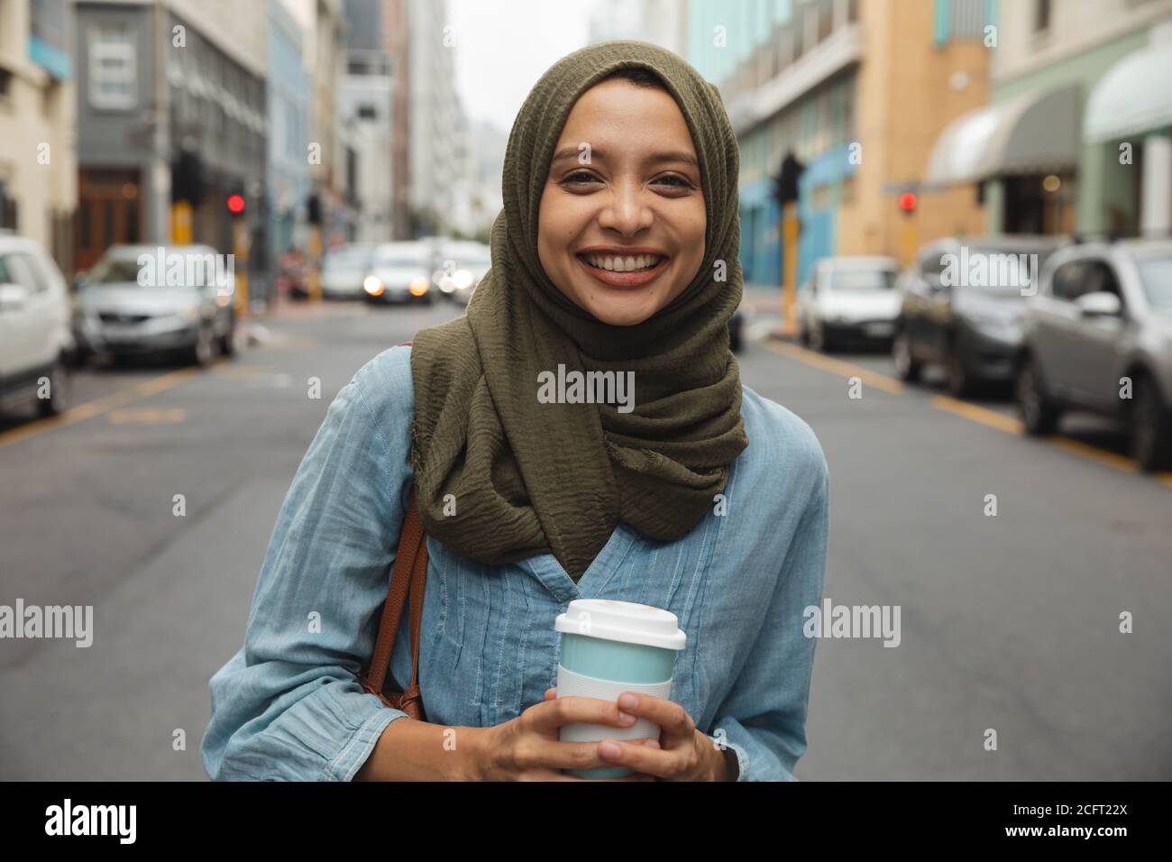 Portrait of woman in hijab with coffee cup smiling on the street Stock Photo