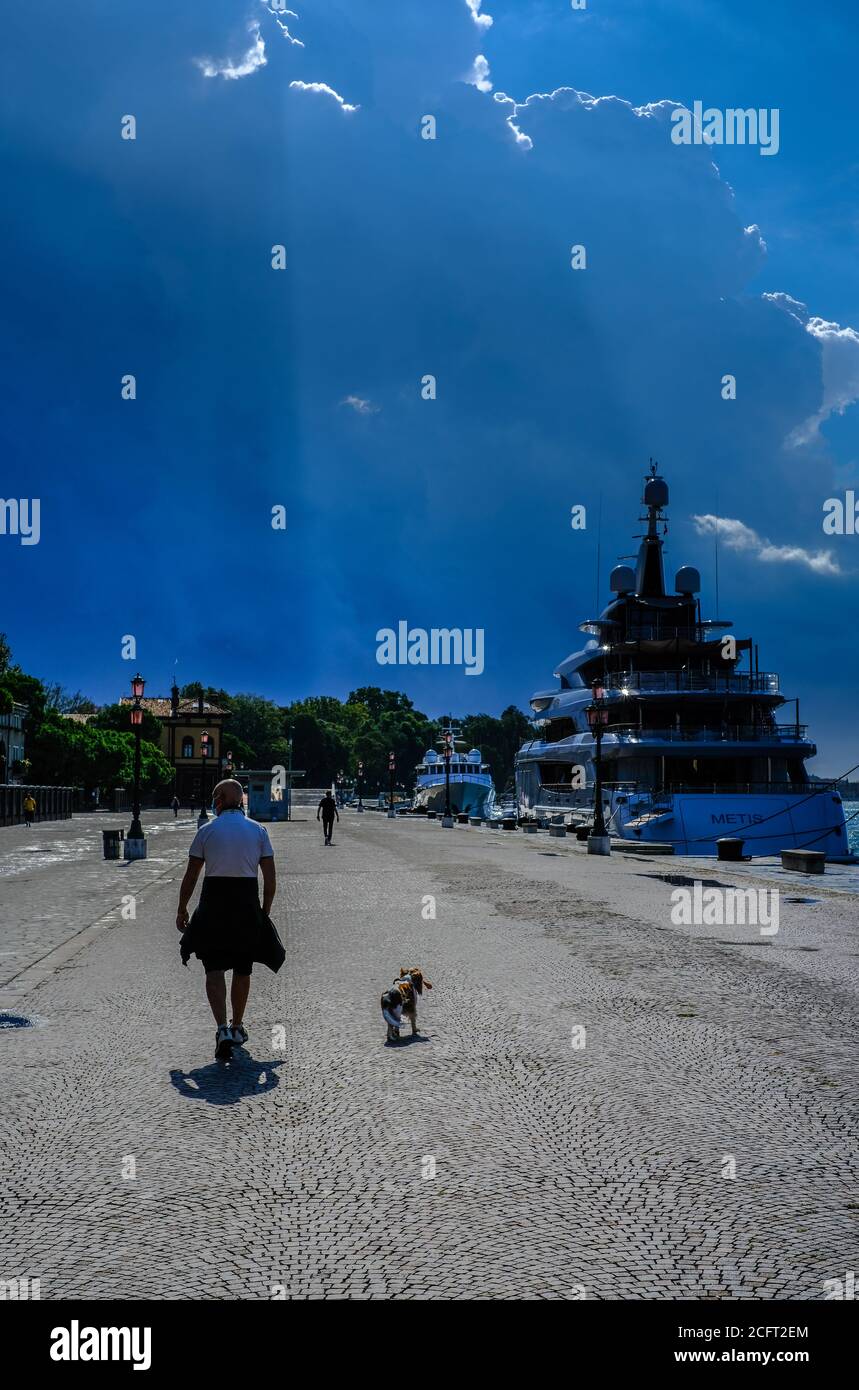 Atmosphere around Venice International Film Festival  on Monday 7 September 2020 at Giardini della Biennale, Venice. A man walking his dog by the waterfront on the wet streets. Picture by Julie Edwards. Stock Photo