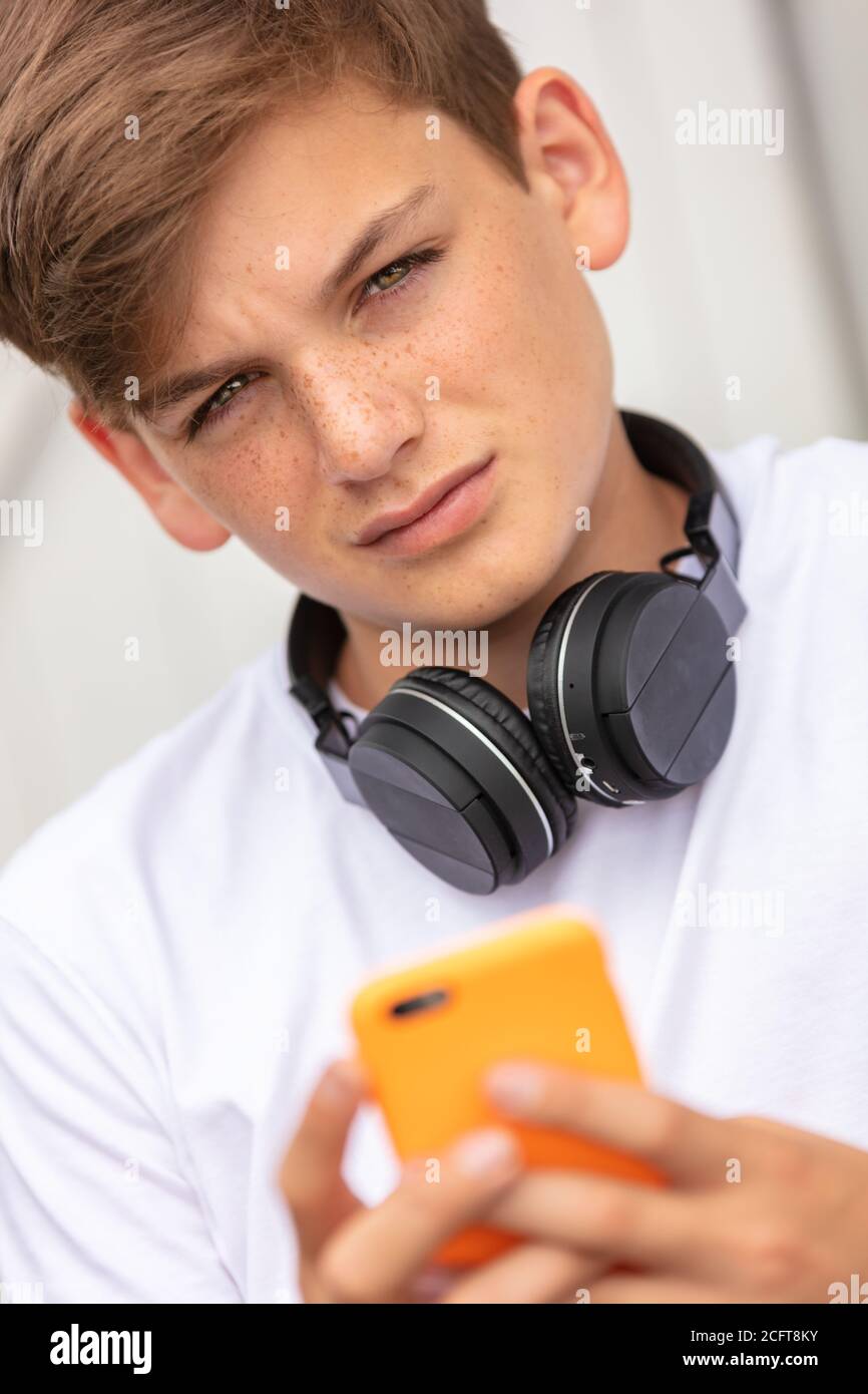 Boy teenager teen male child outside using his mobile cell phone and bluetooth wireless headphones for social media Stock Photo