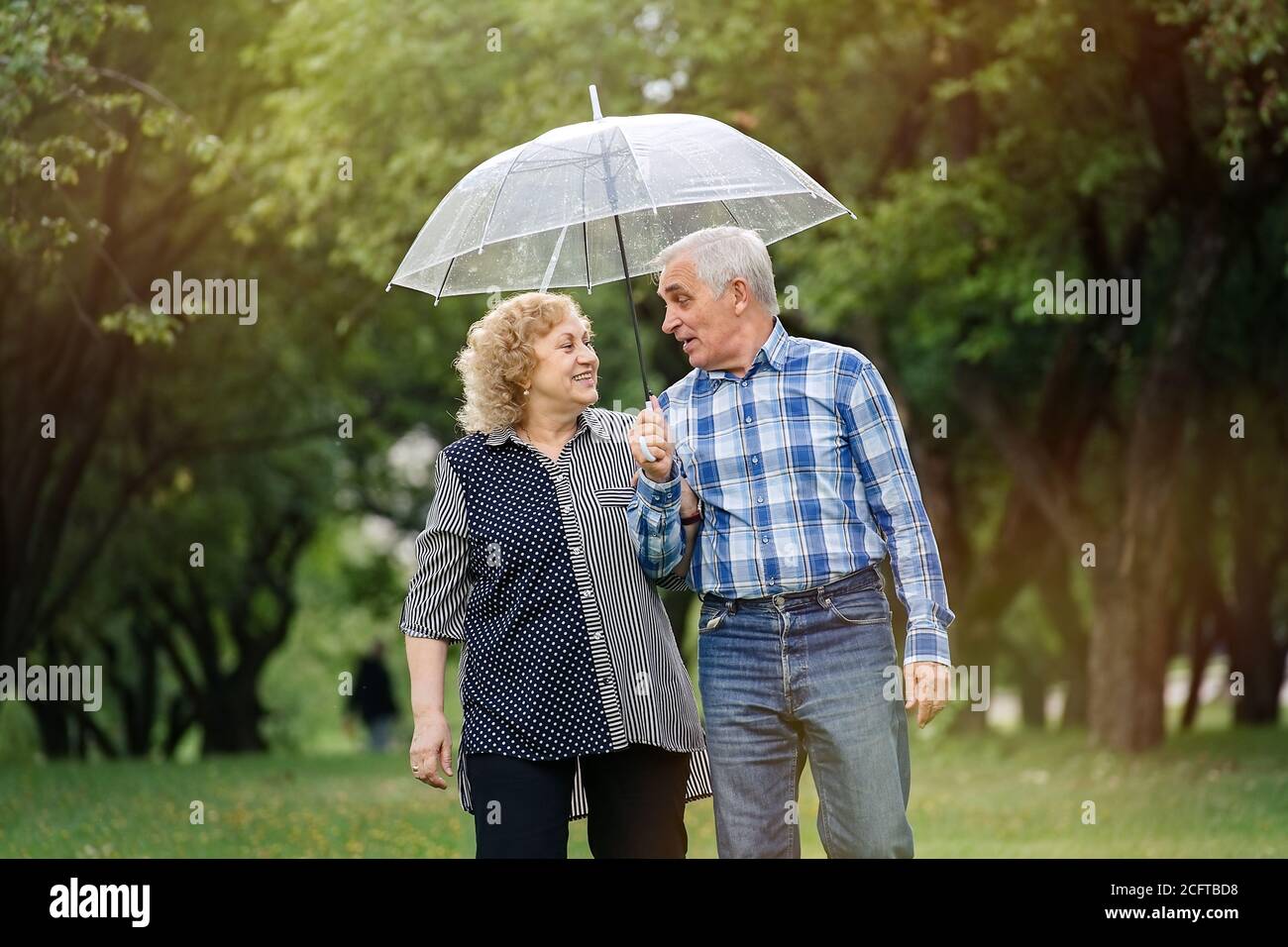 Happy senior couple walking in park during rain under umbrella Stock ...