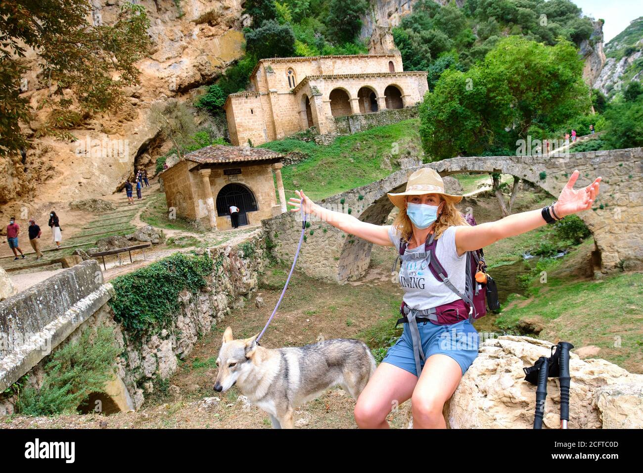 Hiker mature young woman with a face mask and a dog close to an old chapel. Stock Photo