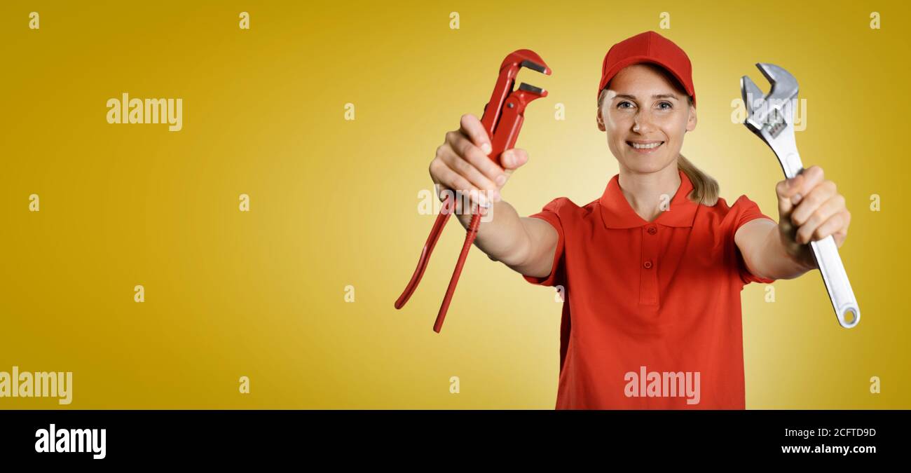 handywoman in red uniform with tools in hands on yellow background with copy space Stock Photo