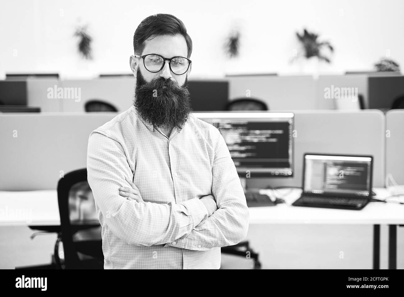 Confident computer programmer developer standing in IT office crossing hands on chest, working on a project in software development company or startup Stock Photo