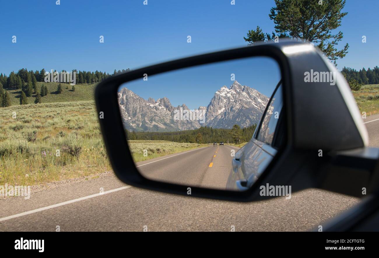 A view of the Grand Teton National Park in the rearview mirror of a car driving in Wyoming Stock Photo