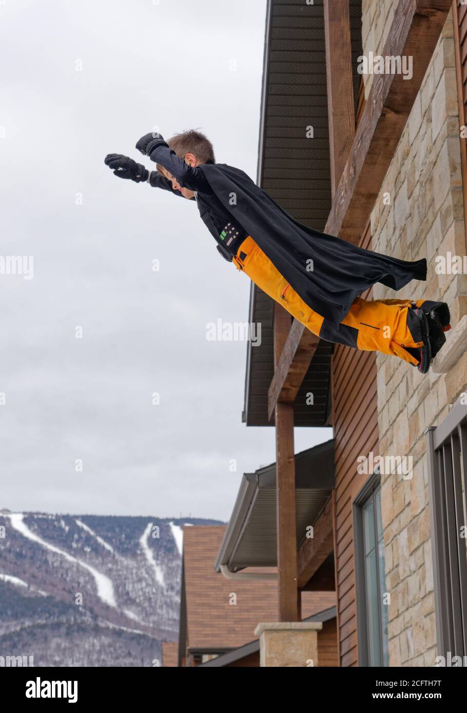 A young boy wearing a superhero cape jumping from the balcony of a house Stock Photo