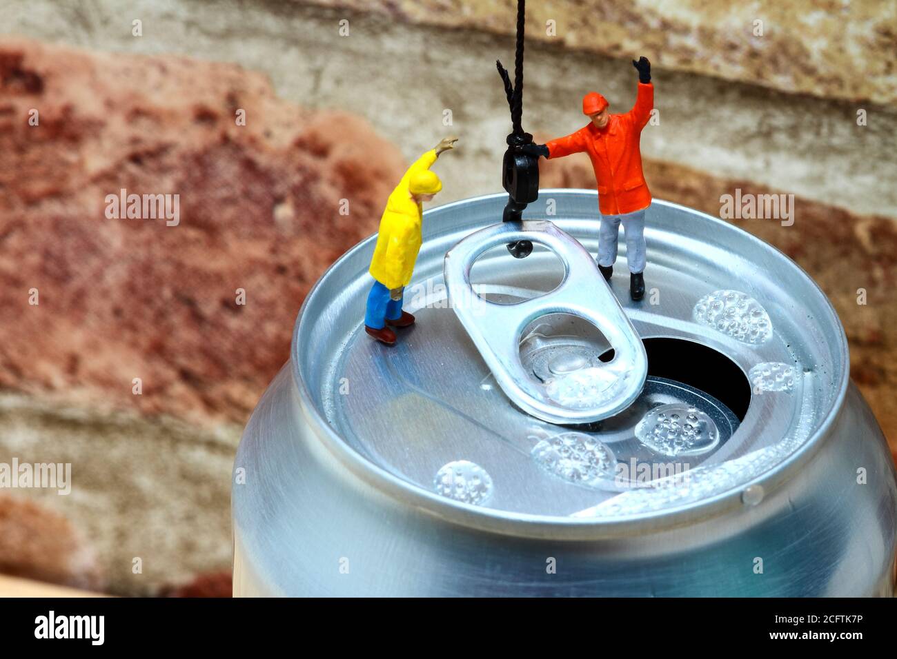 Conceptual image of miniature figure workmen attaching a cranes hook to the ring pull of an aluminium fizzy drinks can Stock Photo