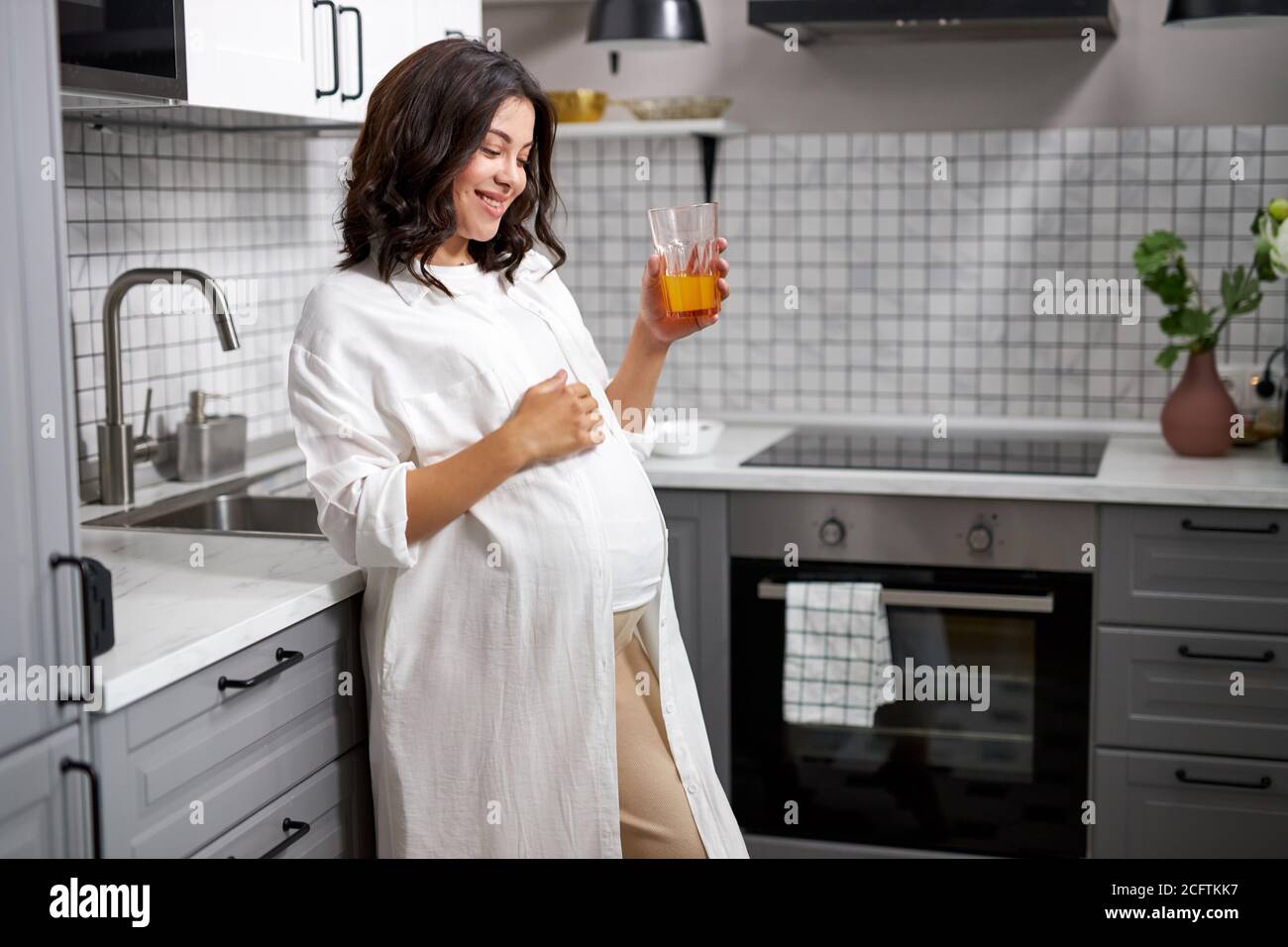 portrait of happy pregnant lady drinking fresh juice in the kitchen ...