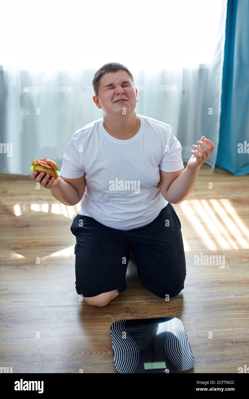 desperate fat boy want to lose weight, but he doesn't stop eating unhealthy food Stock Photo